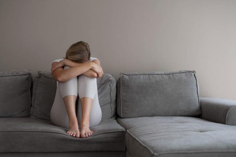 Sad woman sitting alone on grey couch