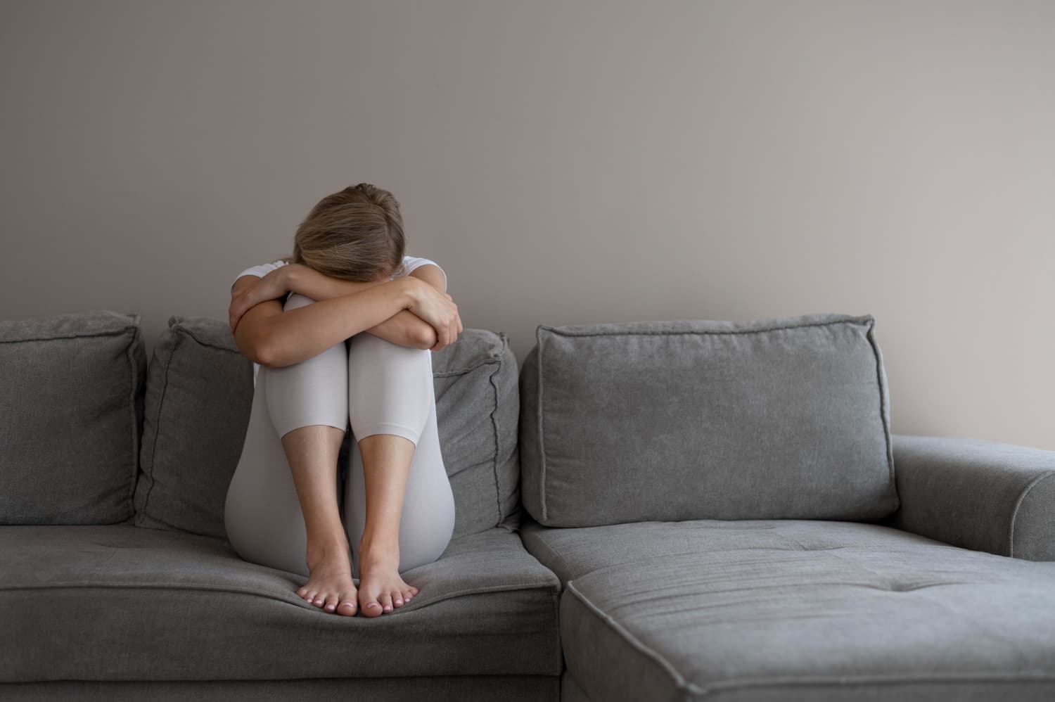 Sad woman sitting alone on grey couch